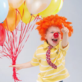 Small jumping kid holding bunch of balloons